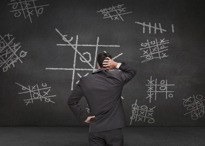 Thoughtful businessman looking at Tictac-toe game drawn on a chalkboard